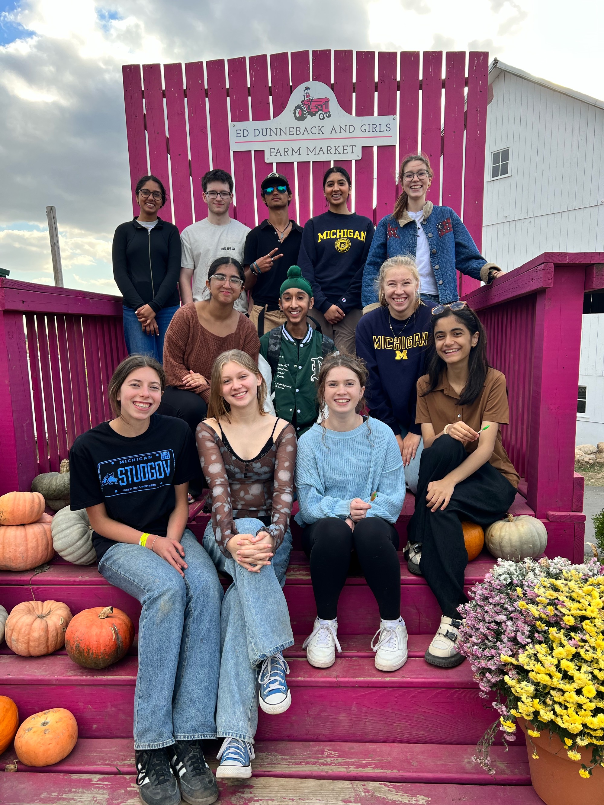 Kaufman Scholars - a group of 13 middle and high school students on an oversized Adirondack chair at an apple orchard.